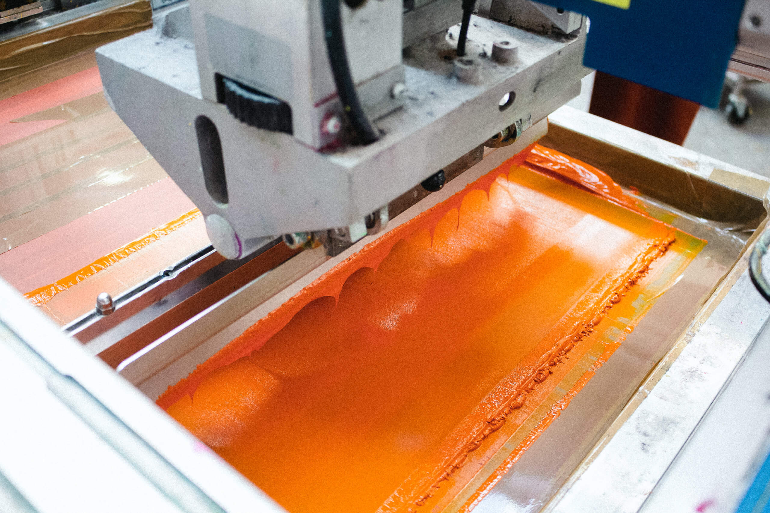 Screen printing process on to t-shirts. Orange ink being printed.